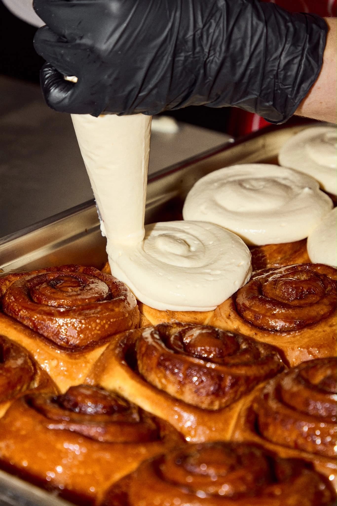 Cream cheese frosting being piped onto cinnamon rolls at Rise & Bun Soho